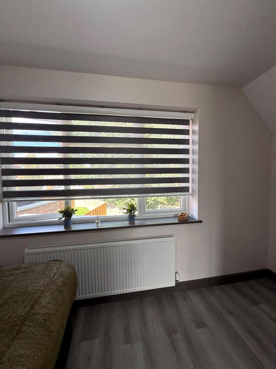 Charcoal day and night blind across a wide window with a garden view