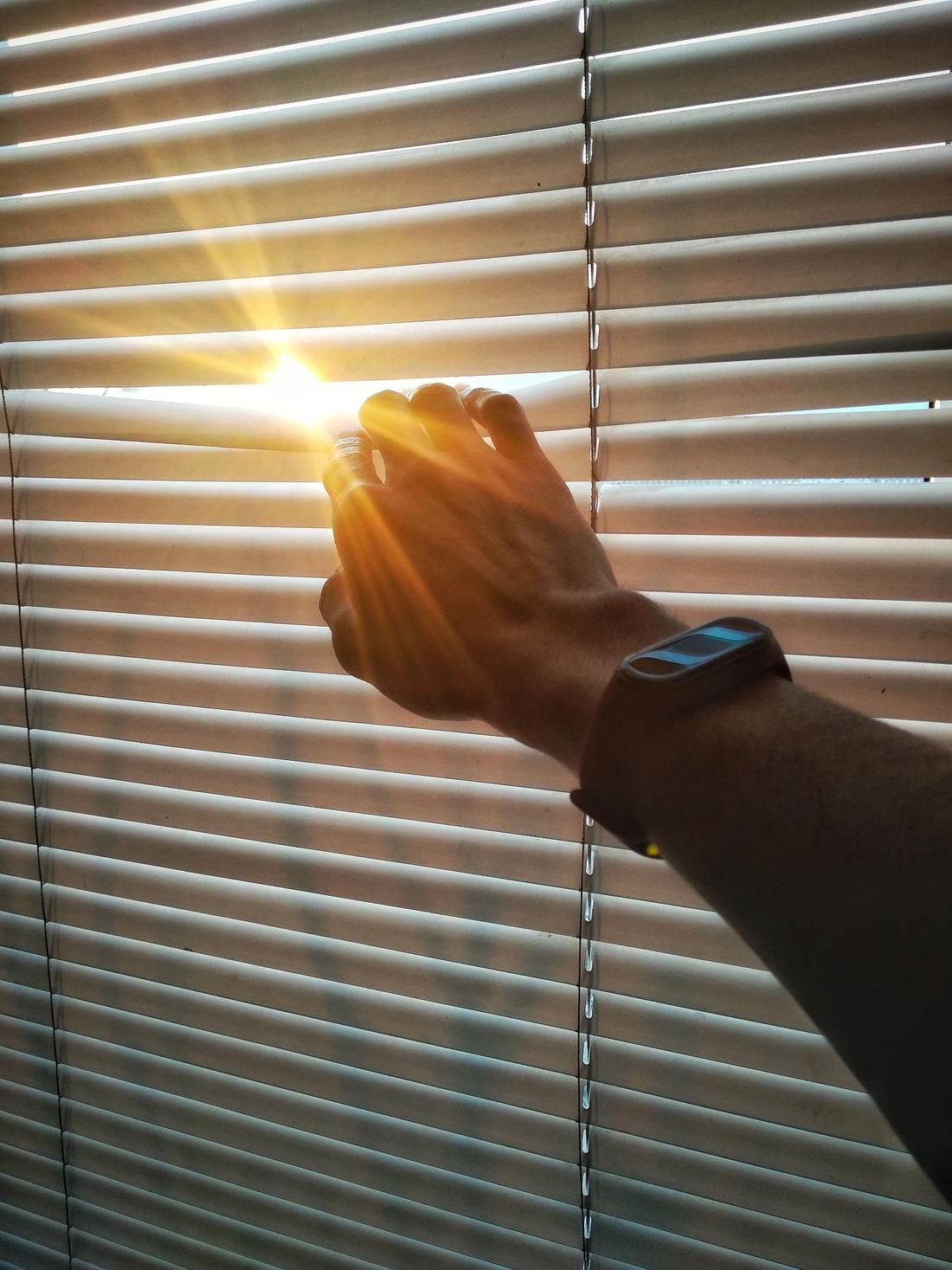 A hand opening a venetian blind to let in the morning sun
