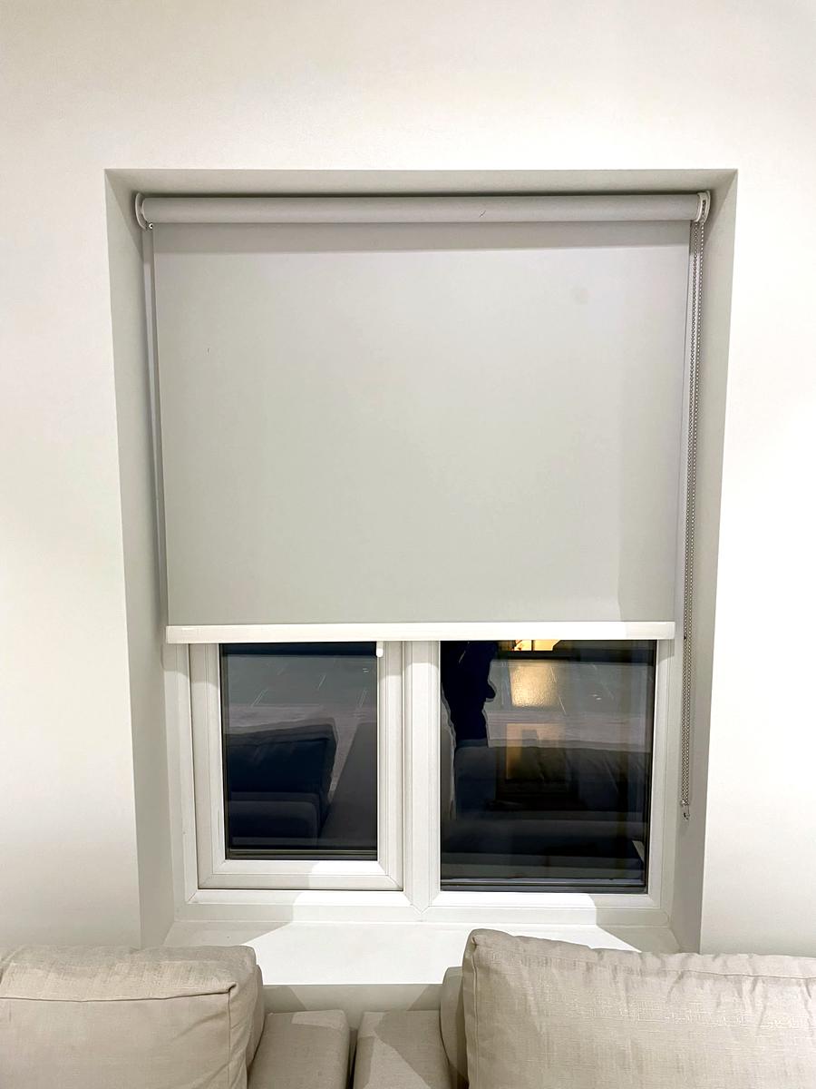 Grey roller blind fitted inside a deep window recess above a sofa
