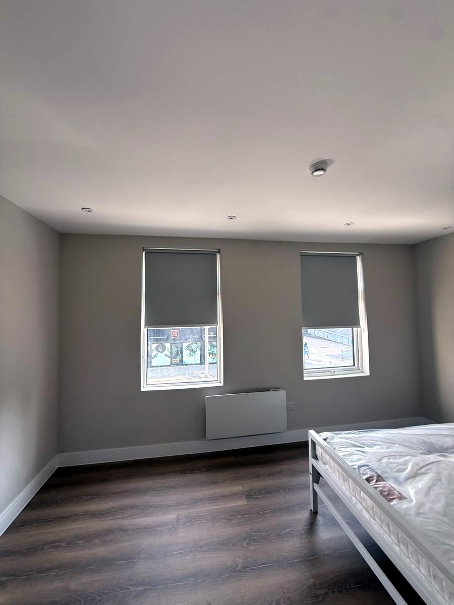 Bedroom with two grey blackout roller blinds on street-facing windows